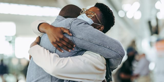 Two people hold each other in a long embrace in an arrivals hall.
